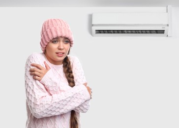 Woman suffering from cold in room with air conditioner on white wall, space for text