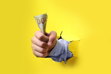 Businessman breaking through yellow paper with money in fist, closeup
