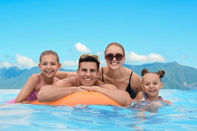 Happy family in outdoor swimming pool at luxury resort with beautiful view of mountains on sunny day