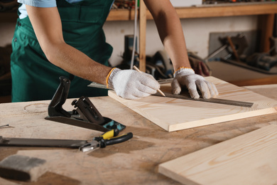 Professional carpenter measuring wooden board in workshop, closeup