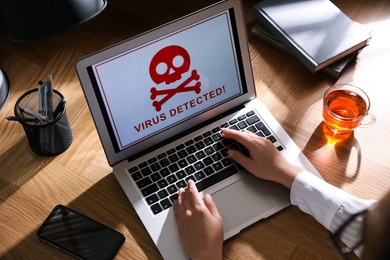Woman using laptop with warning about virus attack at workplace, closeup