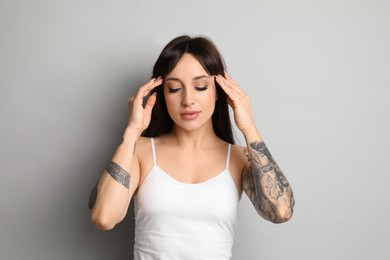 Beautiful woman with tattoos on arms against grey background