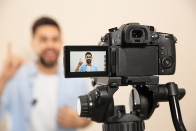 Photo of Young blogger shooting video with camera against beige background, focus on screen