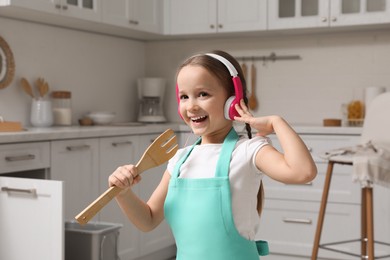 Cute little girl with headphones and fork spatula singing in kitchen