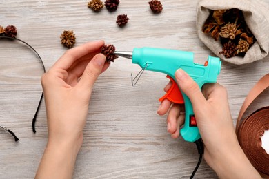 Woman with hot glue gun making craft at wooden table, top view
