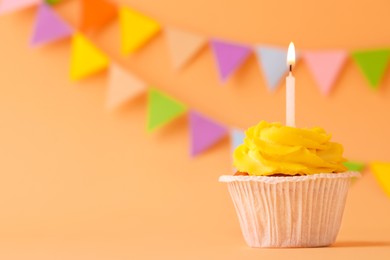 Tasty birthday cupcake with candle on orange table against party flags. Space for text