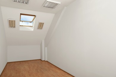 Photo of Light spacious attic room with roof window on slanted ceiling