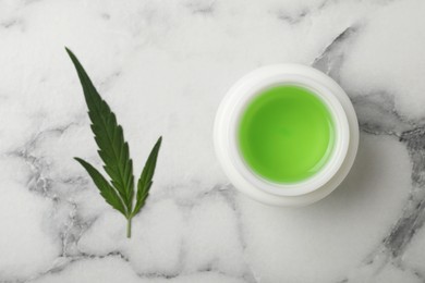 Jar of hemp cosmetics and green leaf on white marble table, flat lay
