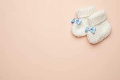 Photo of Knitted baby booties on light pink background, flat lay. space for text