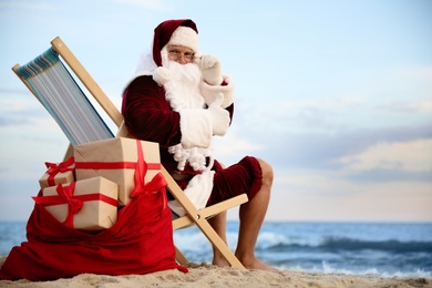 Santa Claus with bag of presents relaxing in chair on beach, space for text. Christmas vacation