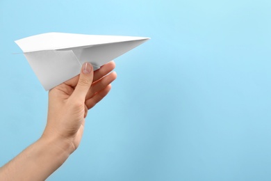 Woman holding paper plane on light blue background, closeup. Space for text
