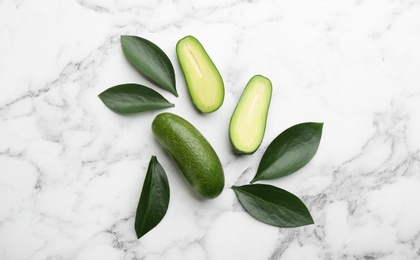 Fresh seedless avocados with green leaves on marble table, flat lay