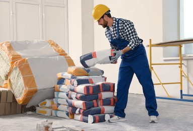 Professional builder in uniform with bag of cement indoors