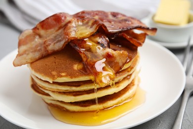 Delicious pancakes with maple syrup and fried bacon on grey table, closeup