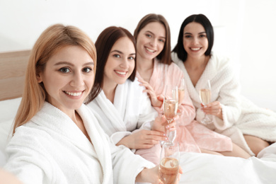 Beautiful young ladies with champagne taking selfie on bed at pamper party. Women's Day