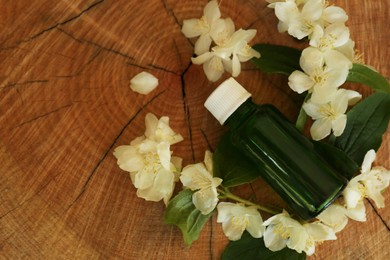 Bottle of jasmine essential oil and white flowers on wooden stump, above view. Space for text