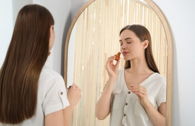Photo of Young woman smelling essential oil near mirror indoors