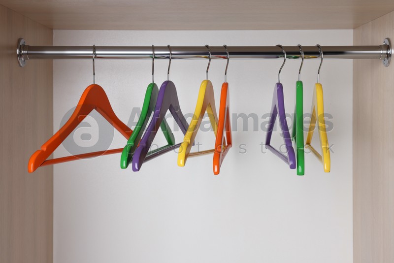 Photo of Set of bright clothes hangers on wardrobe rail