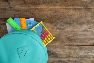 Stylish backpack with different school stationary on wooden table, top view. Space for text