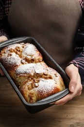 Photo of Woman holding baking pan with delicious yeast dough cake at wooden table, closeup