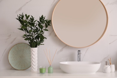 Vase with beautiful branches and toiletries near vessel sink in bathroom. Interior design