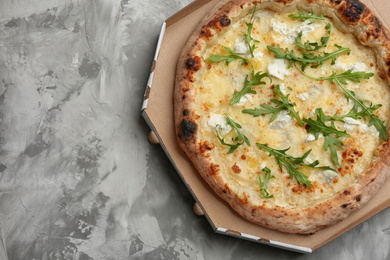 Delicious cheese pizza with arugula in takeout box on grey table, top view