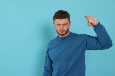 Aggressive young man pointing on light blue background. Space for text