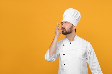 Photo of Mature chef showing delicious gesture on orange background, space for text