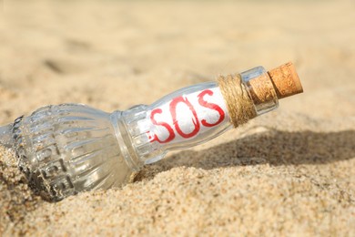 Glass bottle with SOS message on sand, closeup