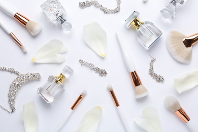 Bottles of perfume, makeup brushes and accessories on white background, flat lay