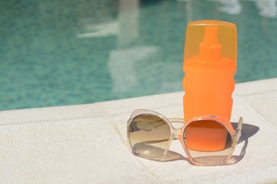 Stylish sunglasses and sunscreen near outdoor swimming pool on sunny day, space for text. Beach accessories
