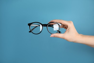 Woman holding glasses on blue background, closeup. Ophthalmologist prescription