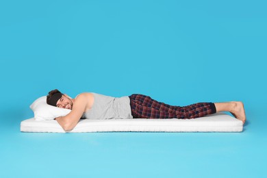 Man in sleeping mask resting on soft mattress against light blue background