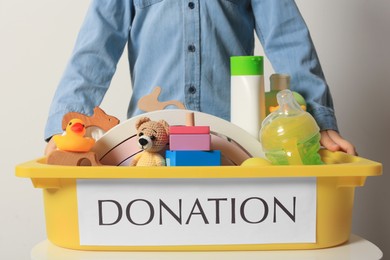 Little boy holding donation box with goods and toys against light background, closeup