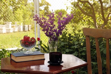 Photo of Beautiful bouquet of wildflowers, drink and book on table in garden