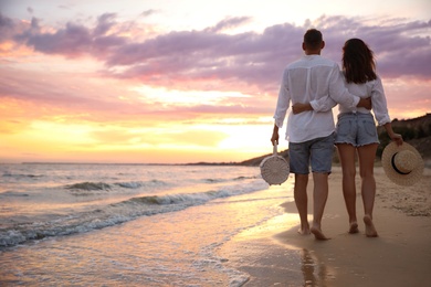 Lovely couple walking on beach at sunset, back view. Space for text