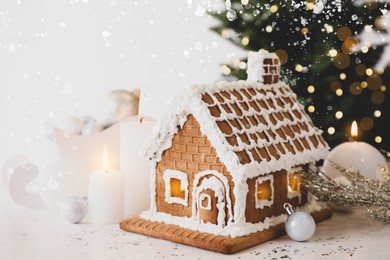 Beautiful gingerbread house decorated with icing and candles on white table