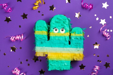 Cactus shaped pinata, streamers and glitter on purple background, flat lay
