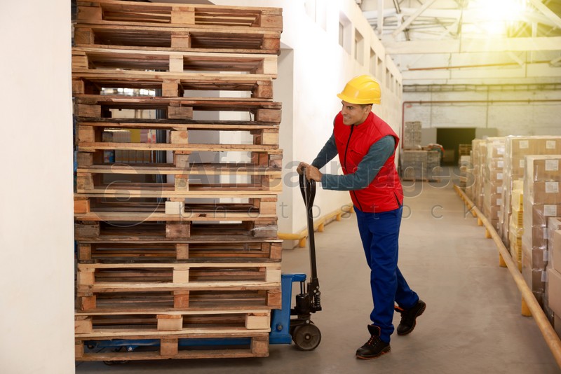 Worker moving wooden pallets with manual forklift in warehouse
