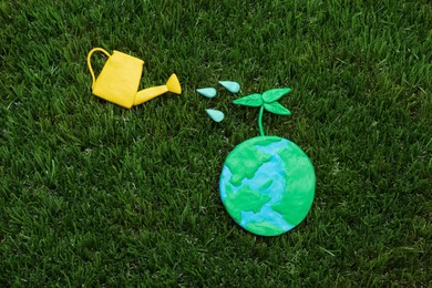 Happy Earth Day. Flat lay composition with plasticine planet and watering can on green grass