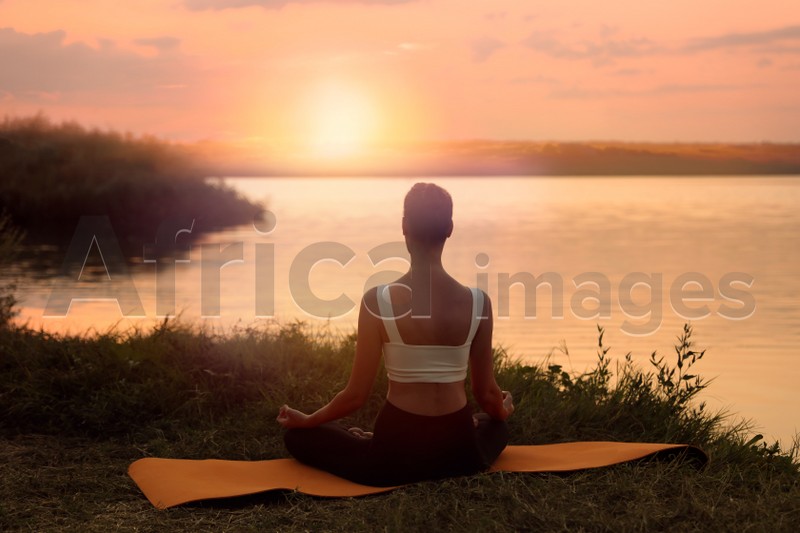 Woman meditating near river in twilight, back view