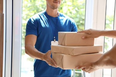 Young courier giving parcels to client in doorway, closeup