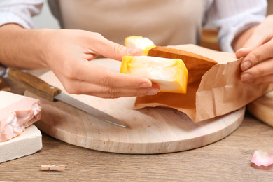 Woman putting natural handmade soap into paper bag at wooden table, closeup