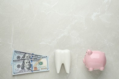 Ceramic model of tooth, piggy bank and dollar banknotes on light grey table, flat lay with space for text. Expensive treatment