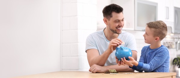 Father and son putting money in piggy bank at home, space for text. Banner design