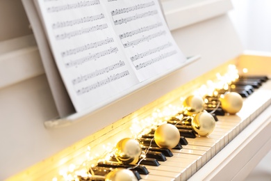 Golden baubles and fairy lights on piano keys, closeup. Christmas music