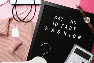 Photo of Black letter board with phrase SAY NO TO FAST FASHION, clothes, wristwatch, shopping bags, hanger and calculator on pink background, flat lay