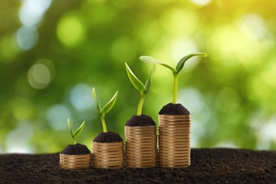 Stacked coins and green seedlings on ground outdoors, bokeh effect. Investment concept