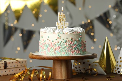Beautiful birthday cake with burning candle and decor on wooden table