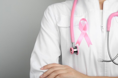 Doctor with pink ribbon and stethoscope on grey background, space for text. Breast cancer awareness